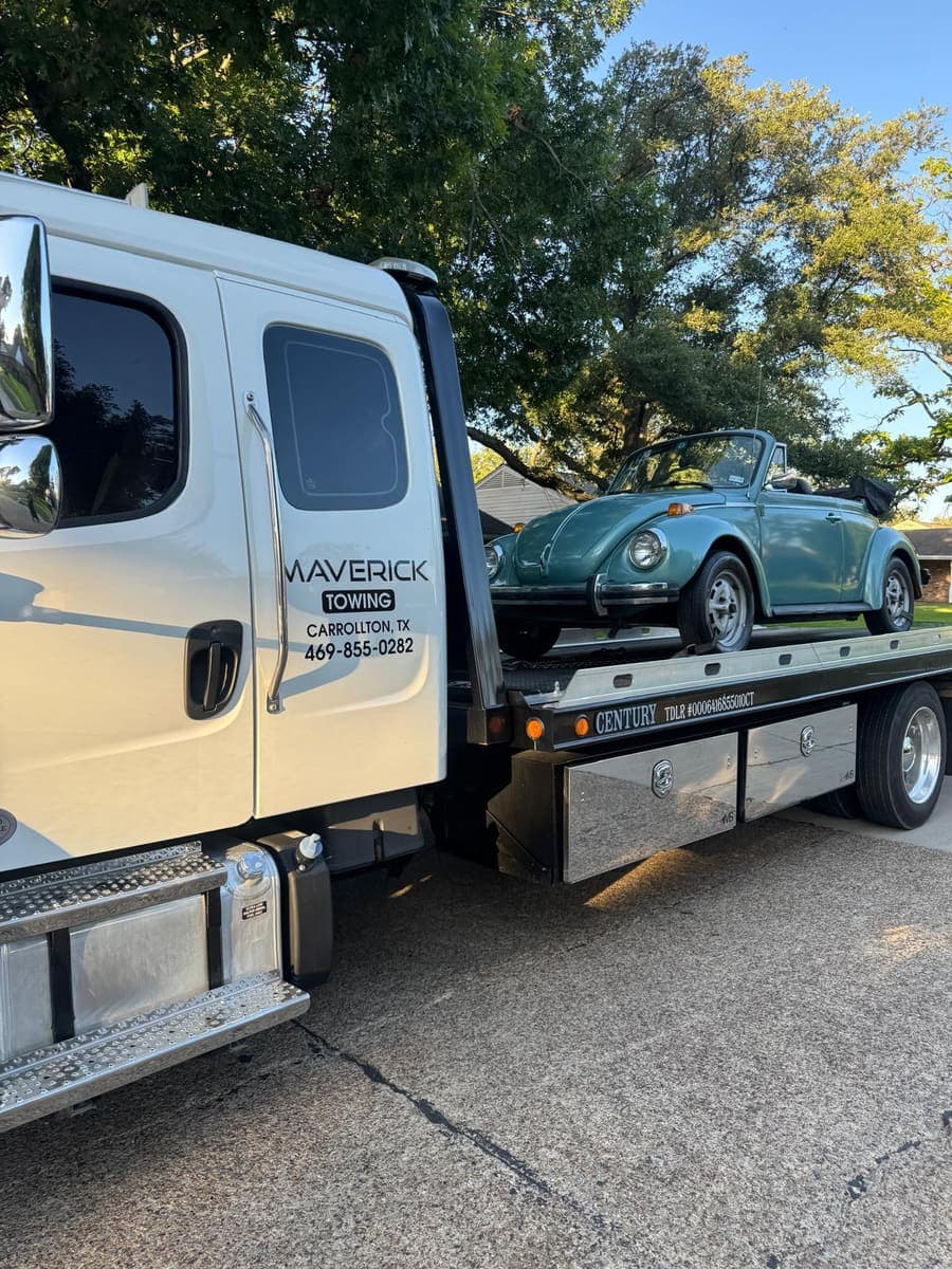 Teal classic Volkswagen Beetle convertible strapped down on a Maverick Towing flatbed under oak trees
